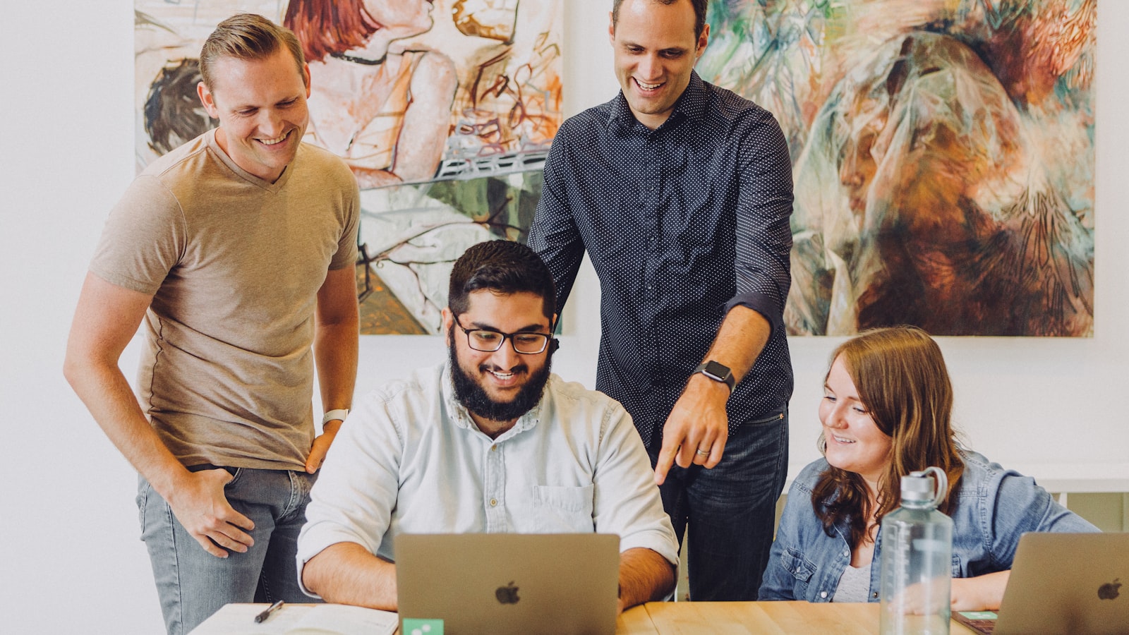 Colleagues gathered around a laptop at a shared desk, working through something together.